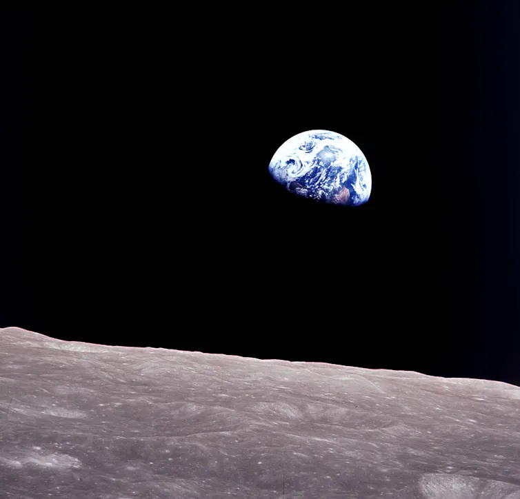 The white and blue cloudy Earth is visible above a gray edge of the Moon's surface