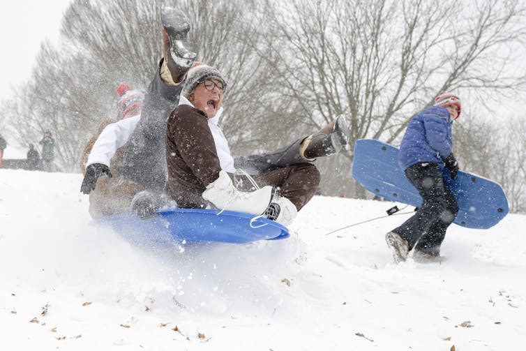 A group of kids scream as they sled down a hillside, legs flying in the air.
