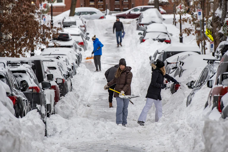 People shovel out cars parked along a road in Boston.