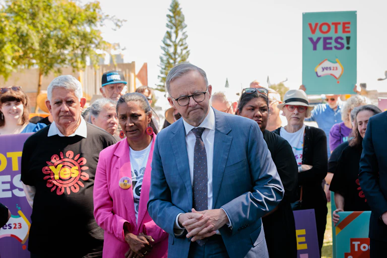Anthony Albanese looking down, frowning, in front of vote yes signs