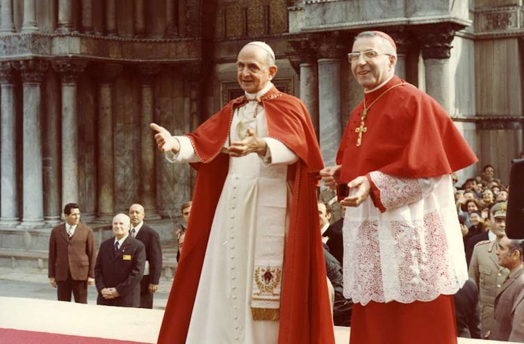 The Pope with a cardinal, both in white and red frocks.