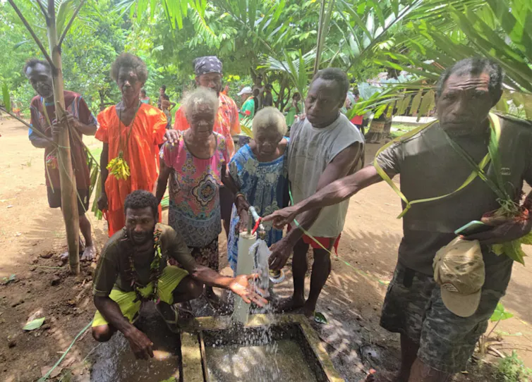 A group of people standing around a water tap