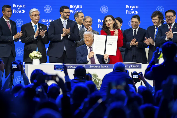 Donald Trump surrounded by world leaderfs, holds up the founding document for his 'Board of Peace' at the World Economic Forum in Davos, January 2026.