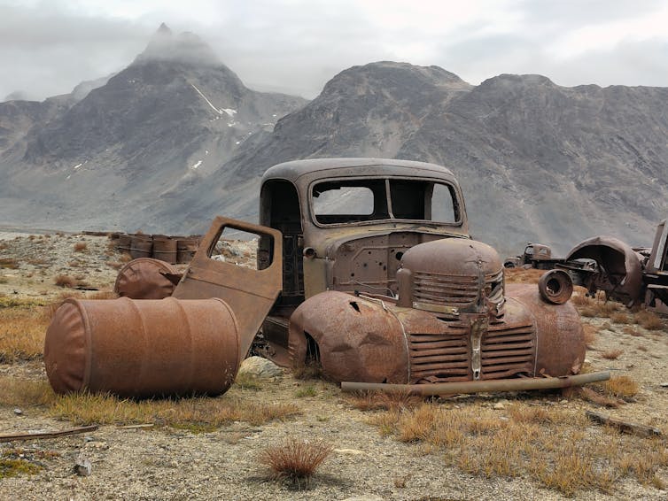A rusting vehicle surrounded by mountains in Greenland.