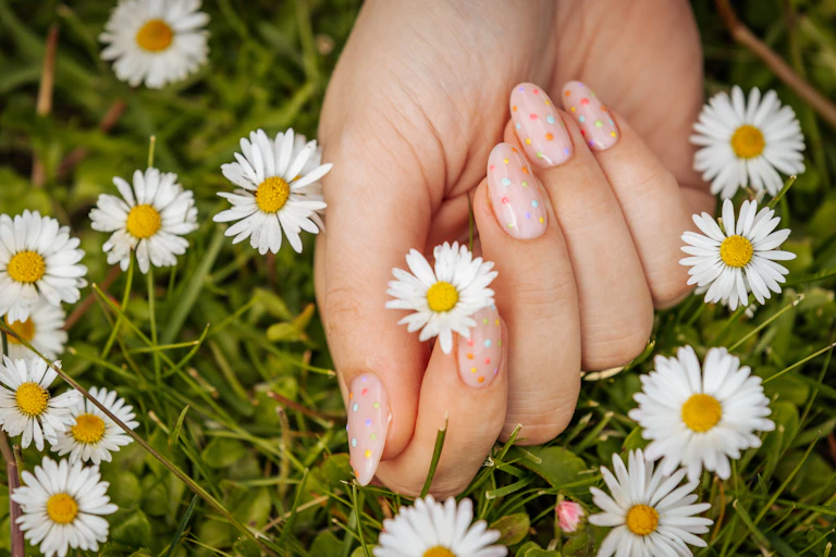 Close up of hand with polka dot fingernails cradling a daisy
