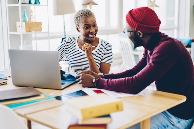 Two people talking at desk with laptop