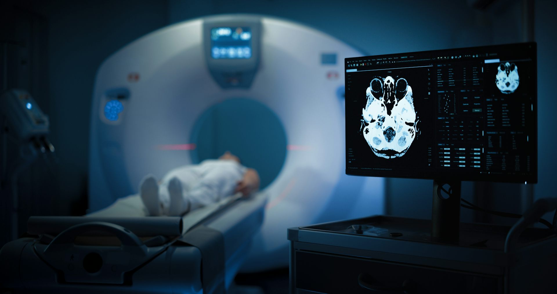 A person lays inside a PET scan machine. A screen to the right shows the ongoing scan of their brain.