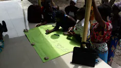 A group of women lean over an A1 sheet of yellow paper, mapping where water and shade can be found on their farms