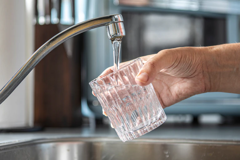 Una mano sostiene un vaso bajo el corro de agua que sale de un grifo de cocina