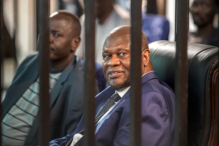 A man seated and looking out through a caged partition.