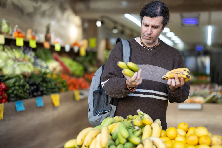 male shopper in a supermarket examining some bananas.