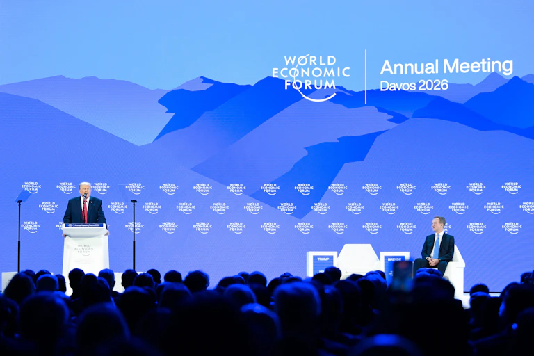 A man in a suit stands at a lectern on a stage.