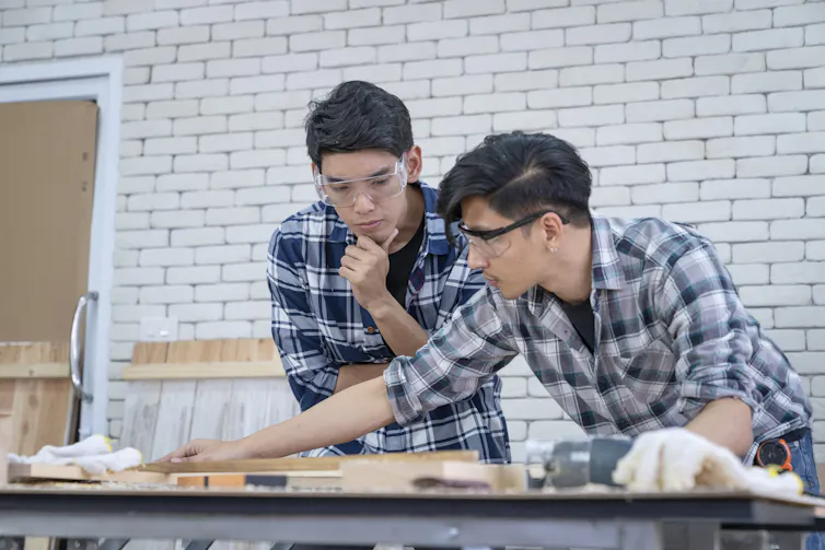 One man watches another closely as he is woodworking