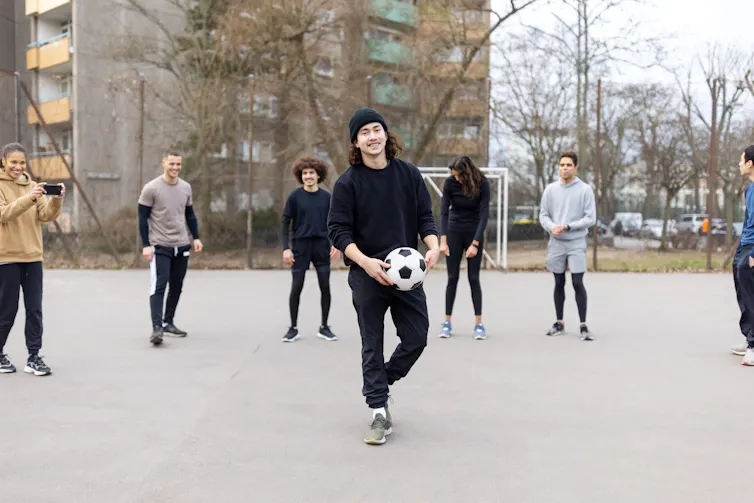 young man on blacktop holding a soccer ball with friends in background