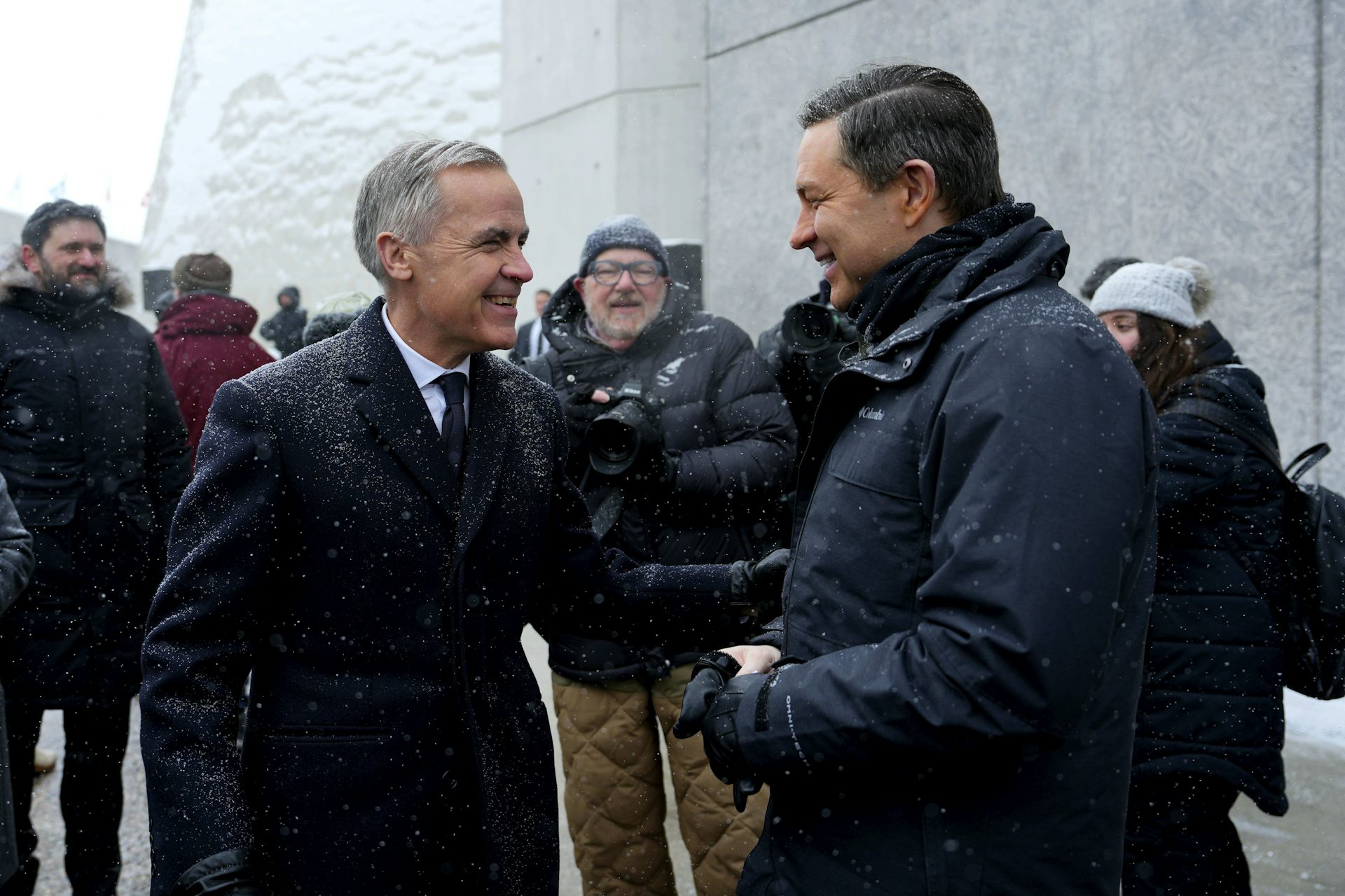 Dos hombres, uno con el pelo corto y gris y el otro con el pelo oscuro, se ríen mientras hablan.