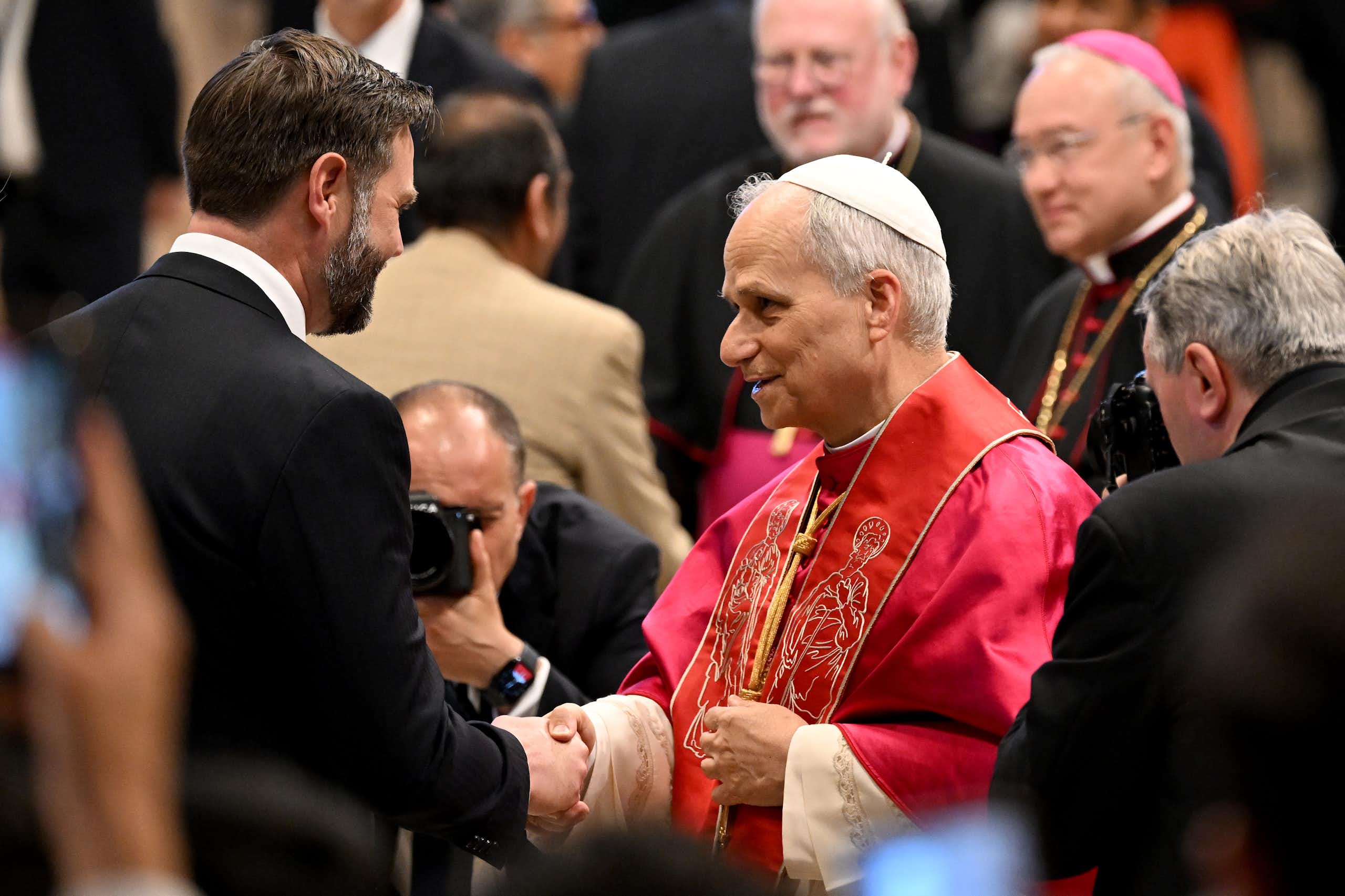 JD Vance, suited, shakes the hand of Pope Leo, in his red frock and cap