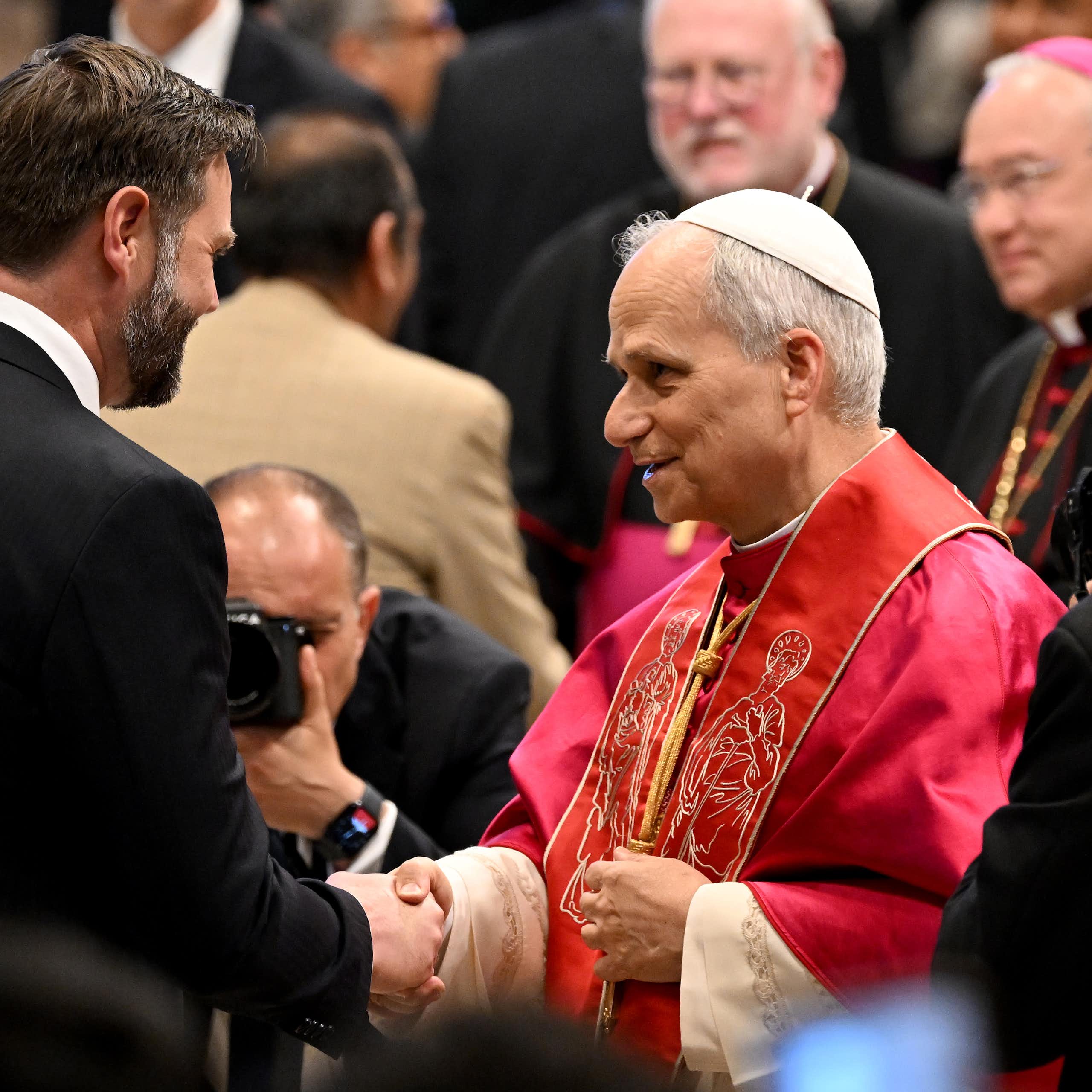 JD Vance, suited, shakes the hand of Pope Leo, in his red frock and cap