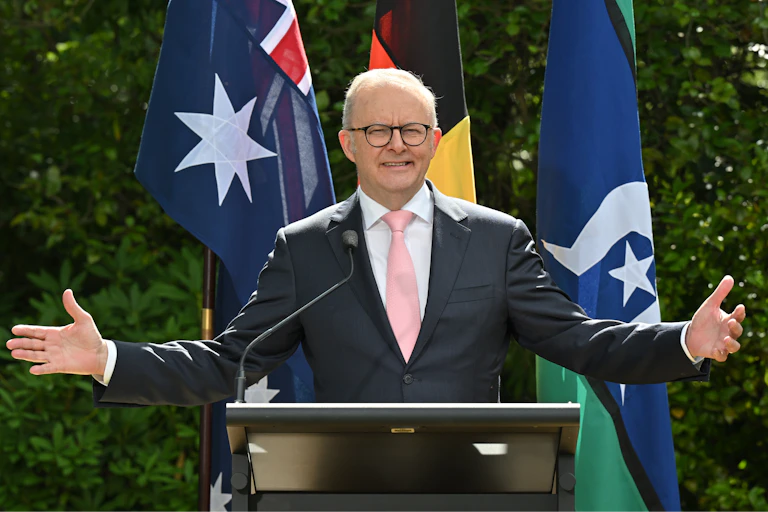 Anthony Albanese with open arms in front of flags.