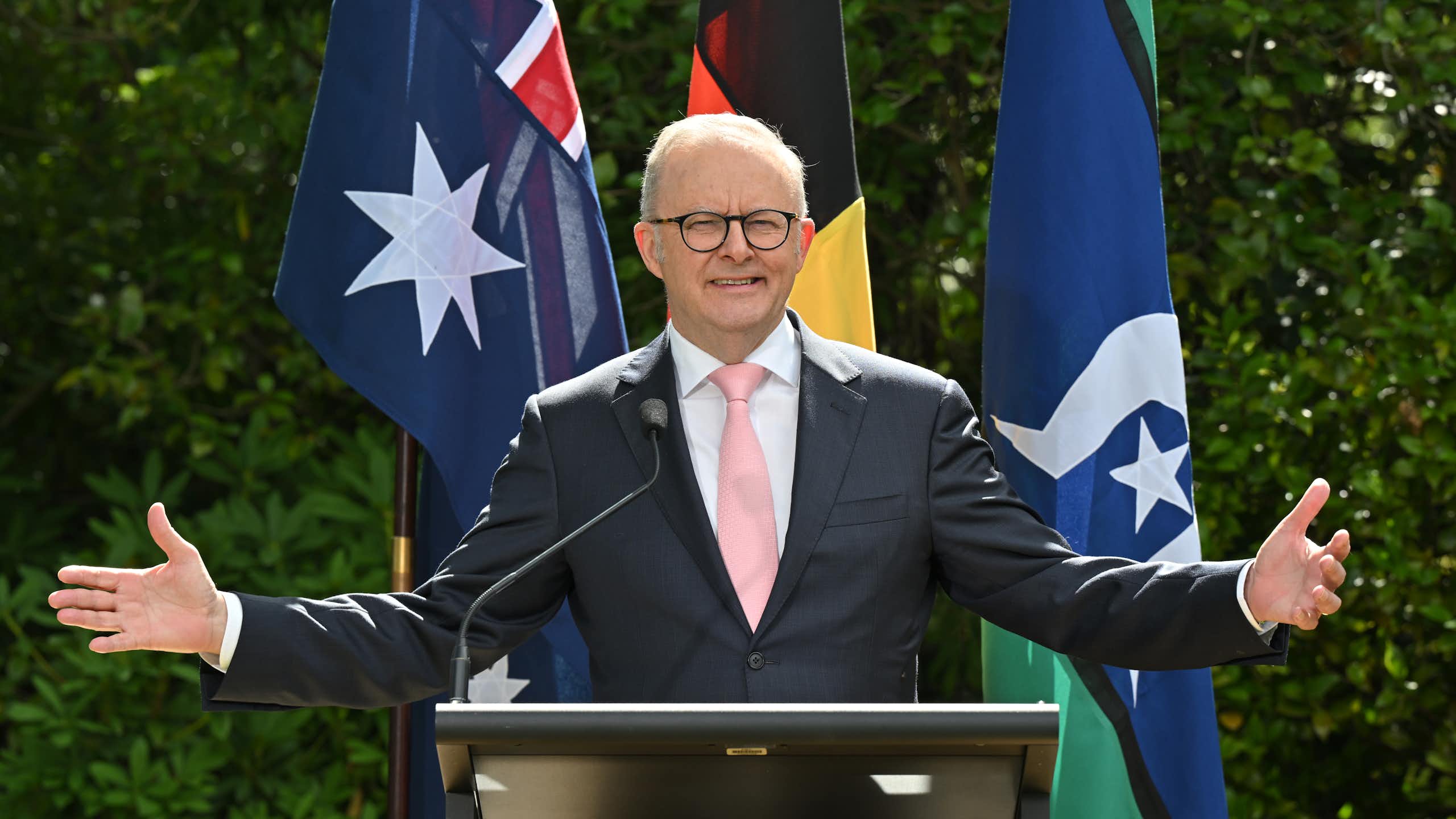 Anthony Albanese with open arms in front of flags.