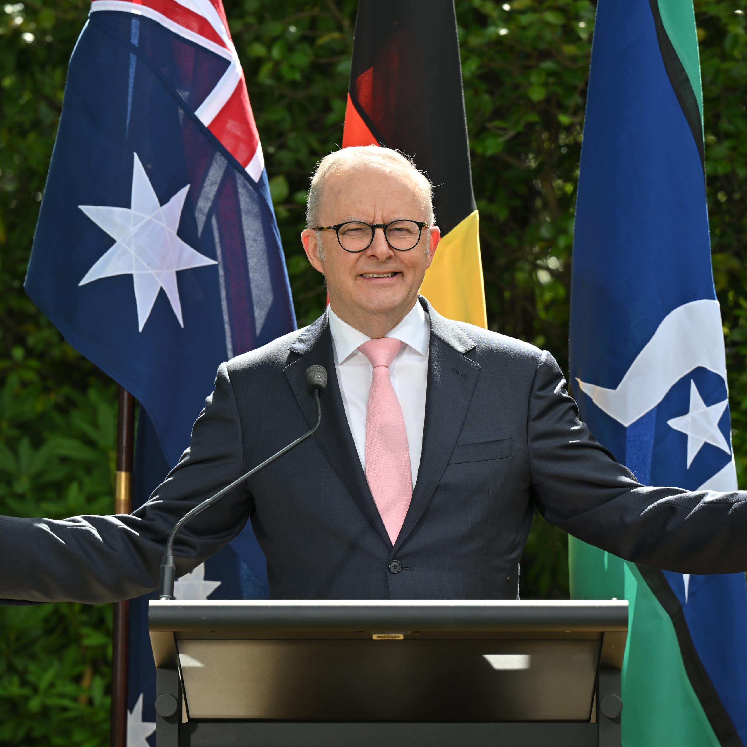 Anthony Albanese with open arms in front of flags.
