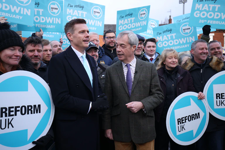 Matt Goodwin and Nigel Farage surrounded by supporters holding Reform signs.