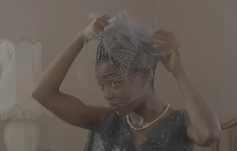 A young African woman in a sepia-toned photo places a delicate hat on her head.