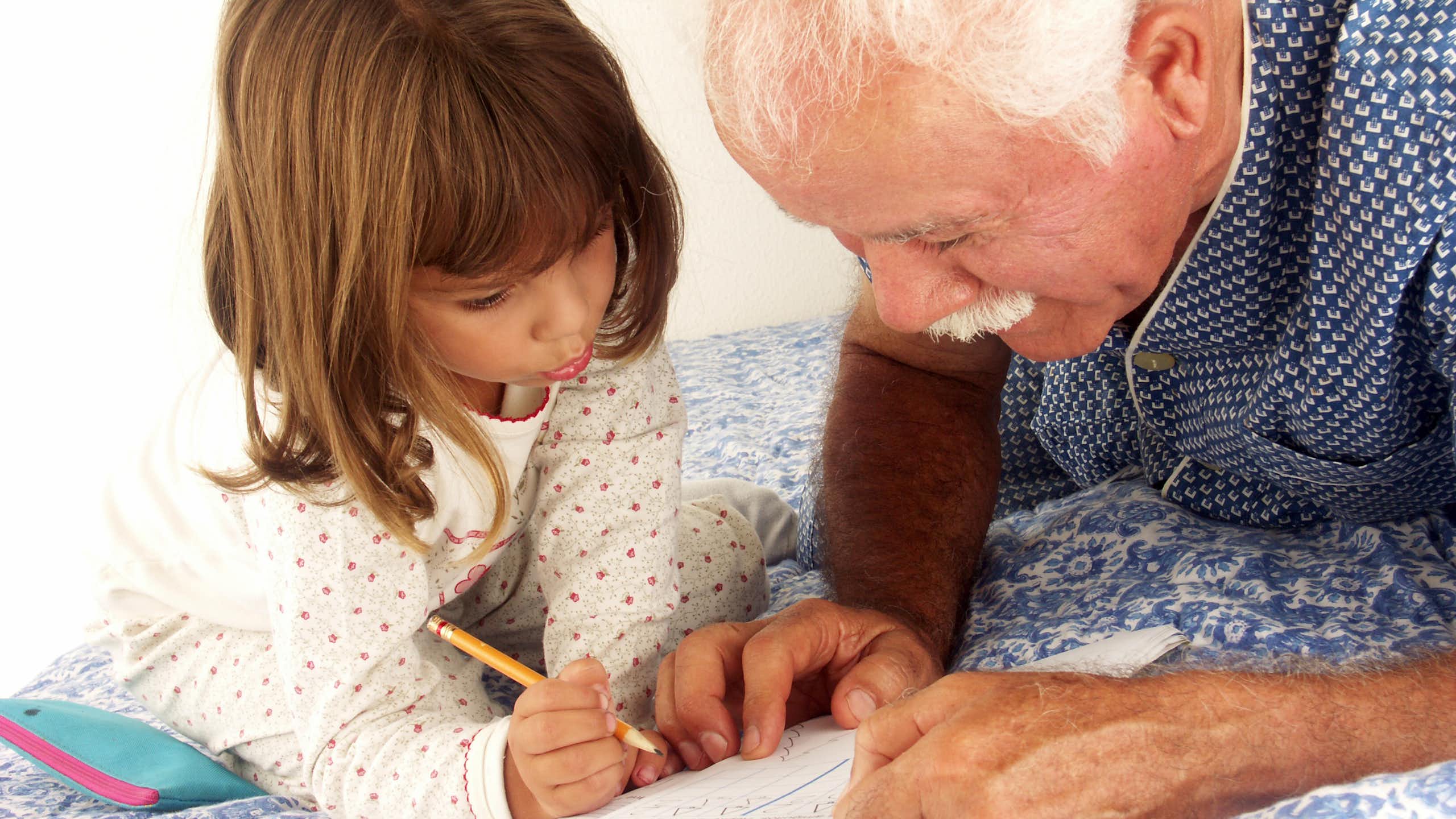Un hombre mayor ayuda a escribir a una niña pequeña.