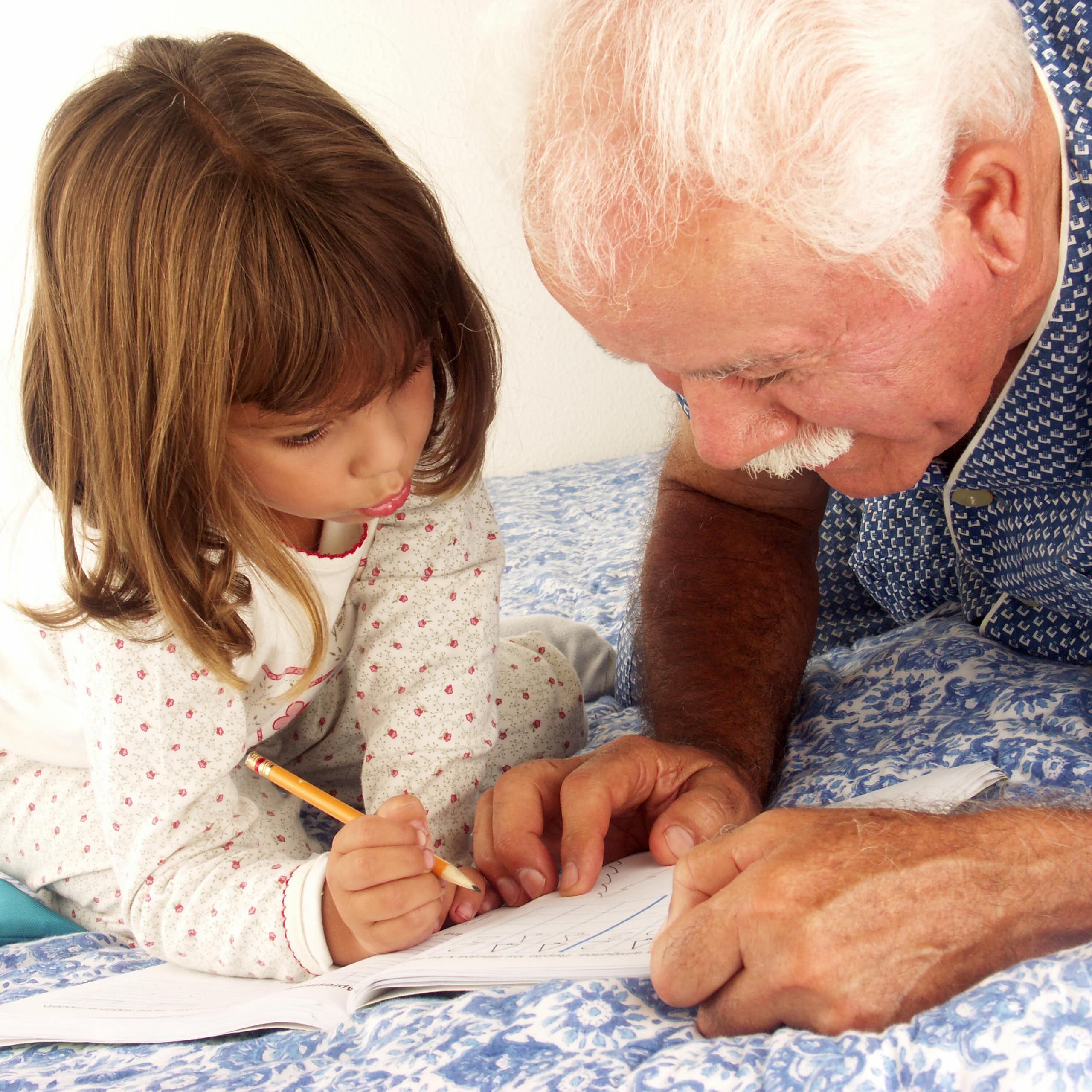 Un hombre mayor ayuda a escribir a una niña pequeña.