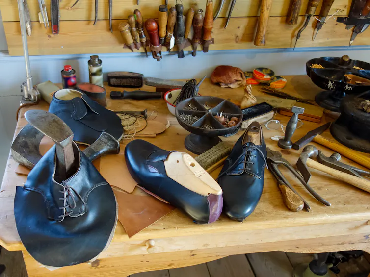 aretesanal shoemaking equipment laid out on a workbench alongside completed and half-made shoes.