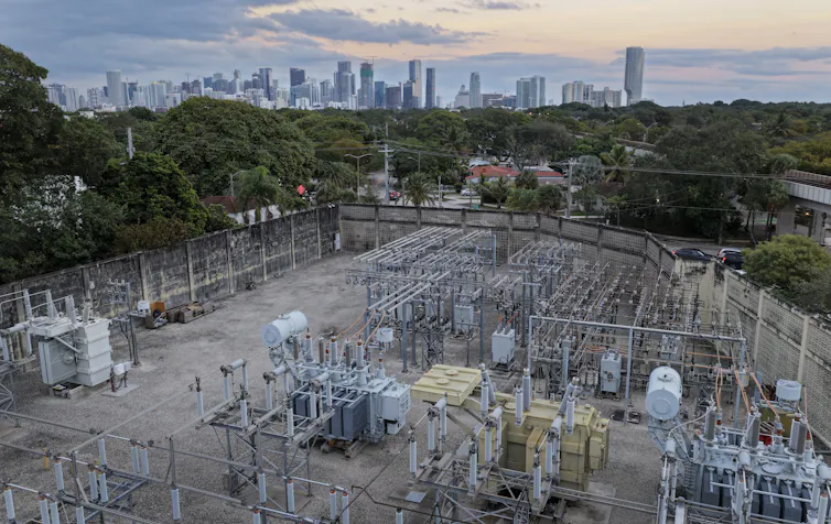 An aerial view of metal equipment and wires with a city skyline in the background.