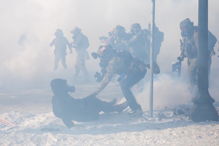 Protesters fight with law enforcement as tear gas fills the air.