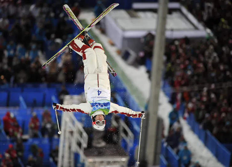 A man on skis hangs upside down in the air mid-flip