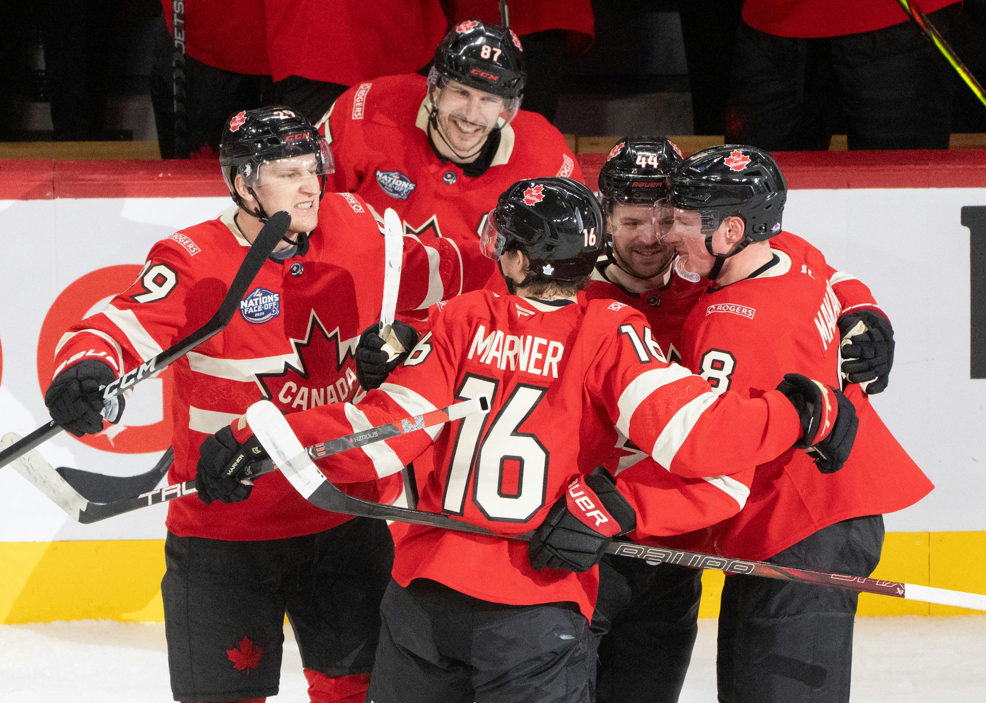 Un grupo de hombres con uniformes rojos de hockey canadiense se abrazan en el hielo.