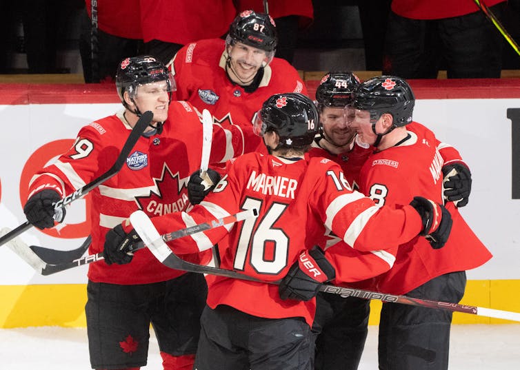 Un grupo de hombres con uniformes rojos de hockey canadiense se abrazan en el hielo.