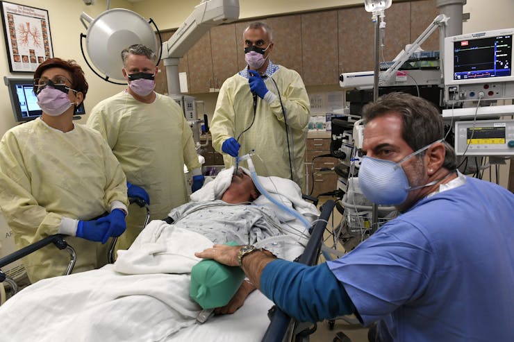 Medical personnel in protective gear stand around a surgical patient during a procedure.
