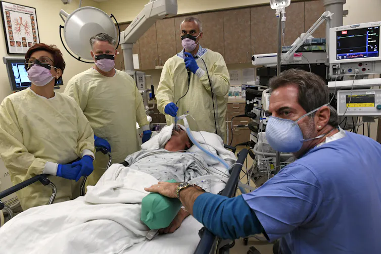 Medical personnel in protective gear stand around a surgical patient during a procedure.