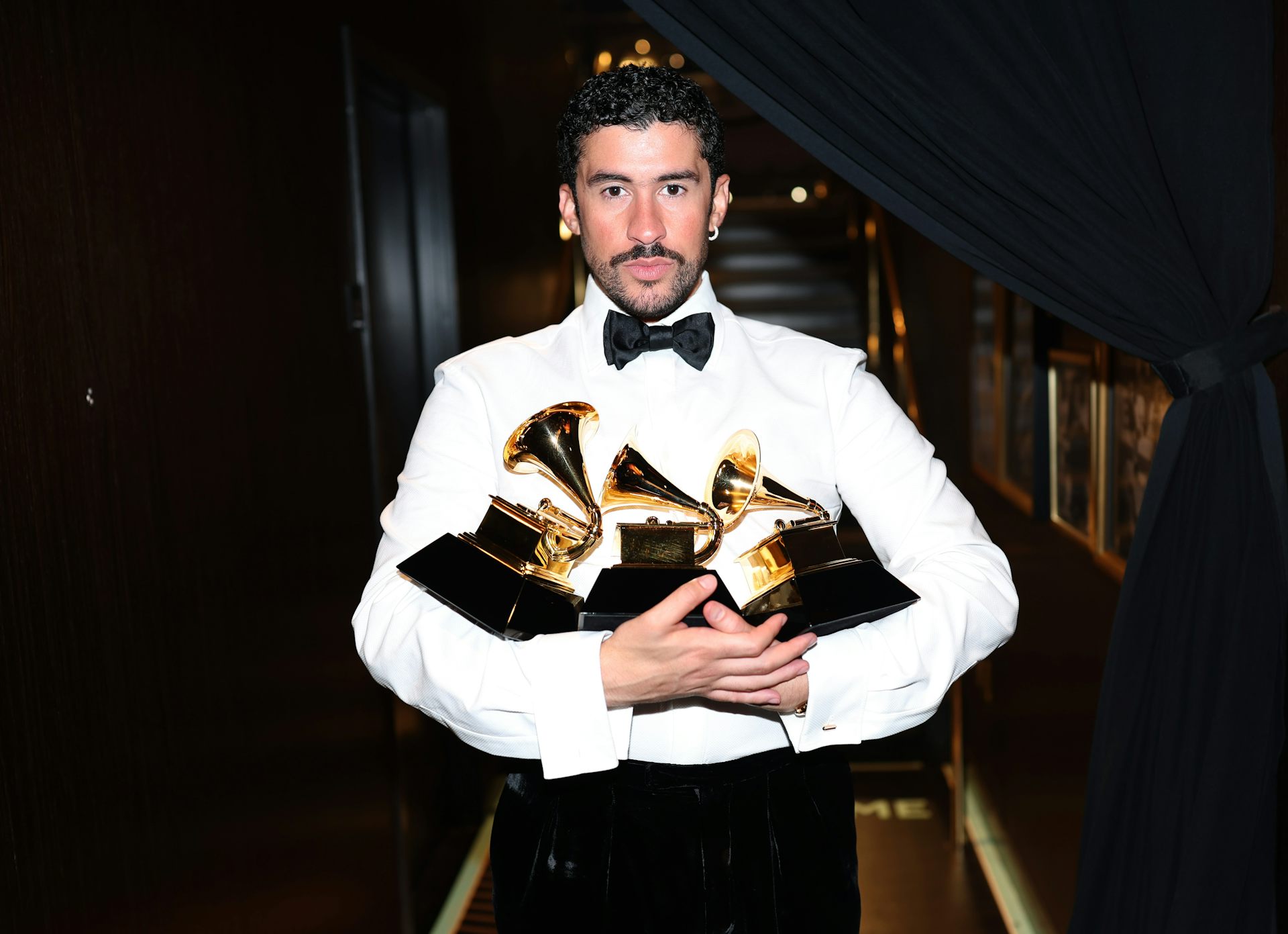 A man in a bowtie holds three trophies.