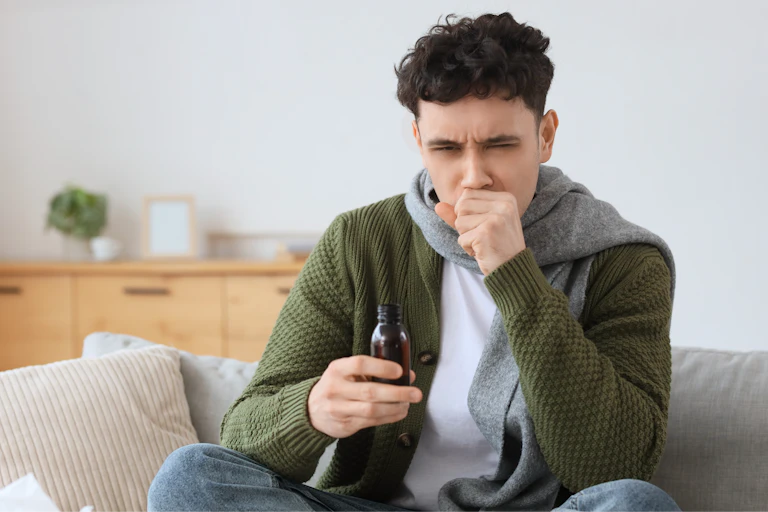 Young man with bottle of cough syrup sitting on sofa in living room