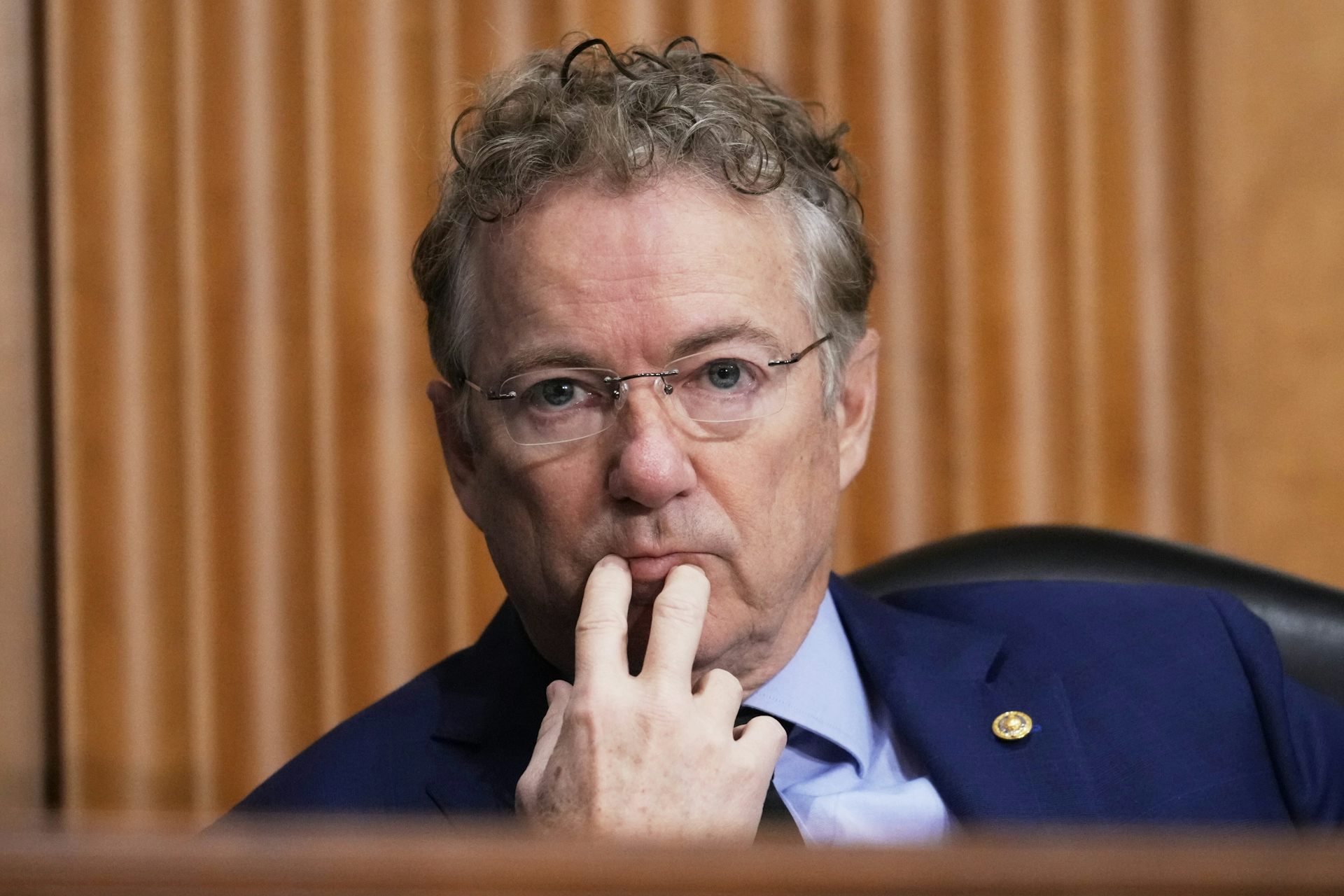 Sen. Rand Paul touches two fingers to his lips as he listens to someone testifying.
