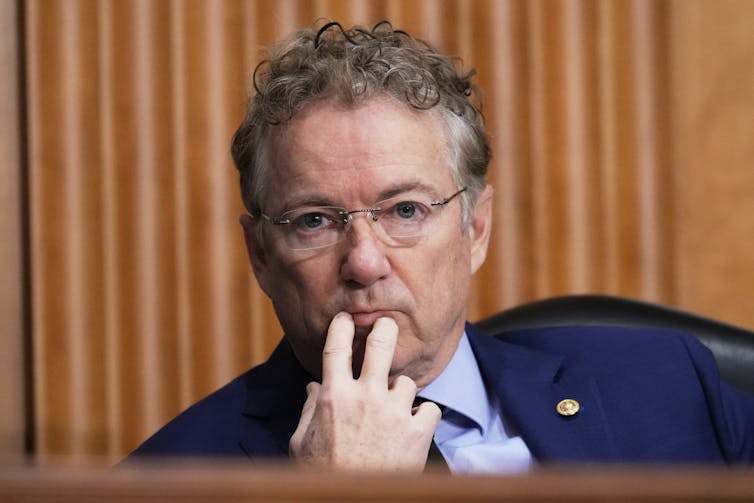 Sen. Rand Paul touches two fingers to his lips as he listens to someone testifying.