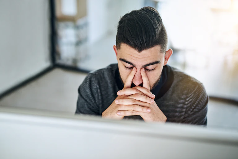 young man sitting at a laptop looking stressed.