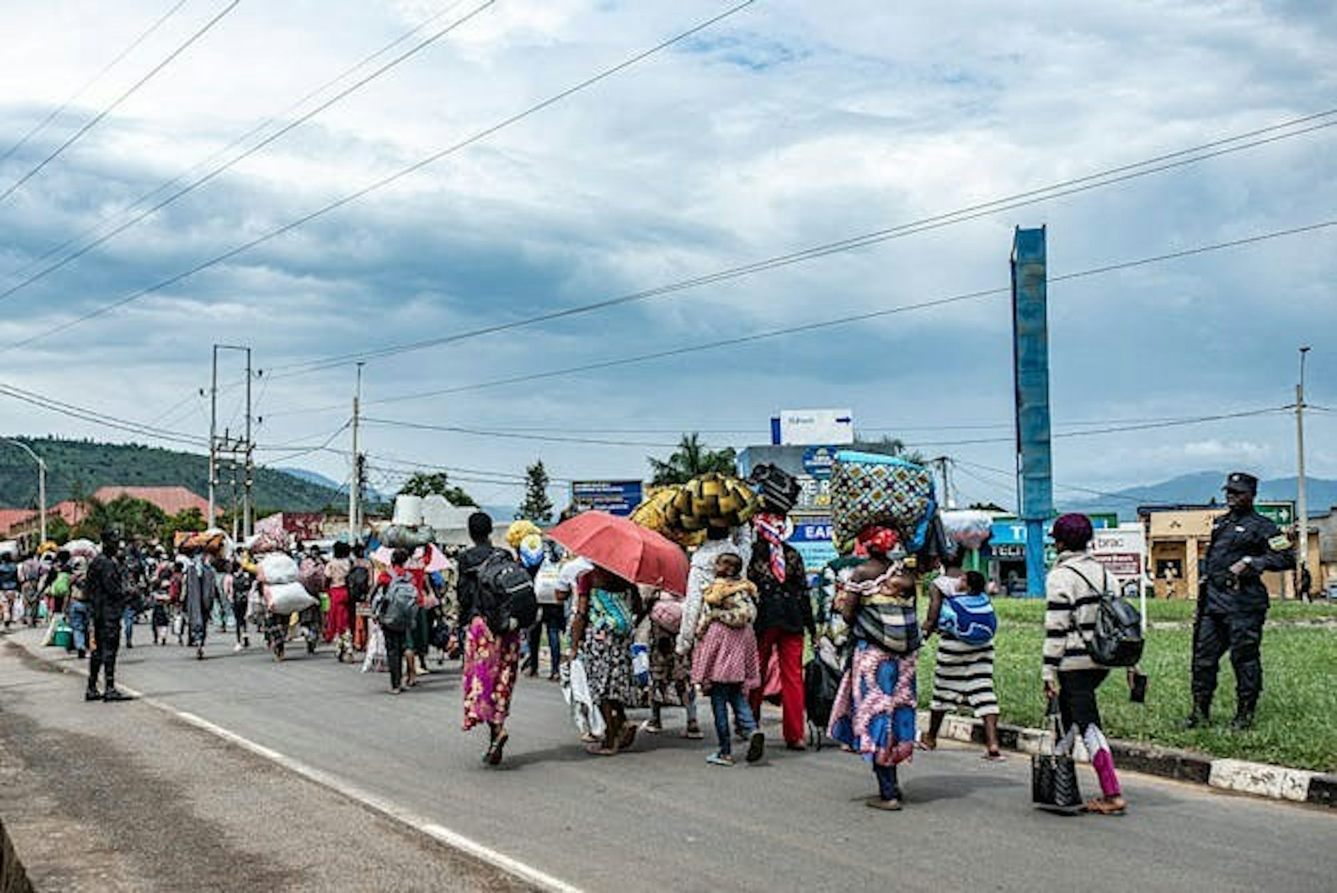 Un groupe de personnes marchant sur une route pavée, transportant des sacs sur leur dos et leur tête.