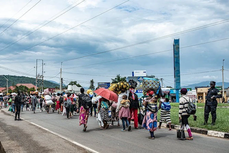 Un groupe de personnes marchant sur une route pavée, transportant des sacs sur leur dos et leur tête.