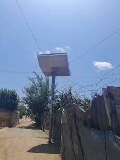 A pole between shacks with a big solar panel on top.