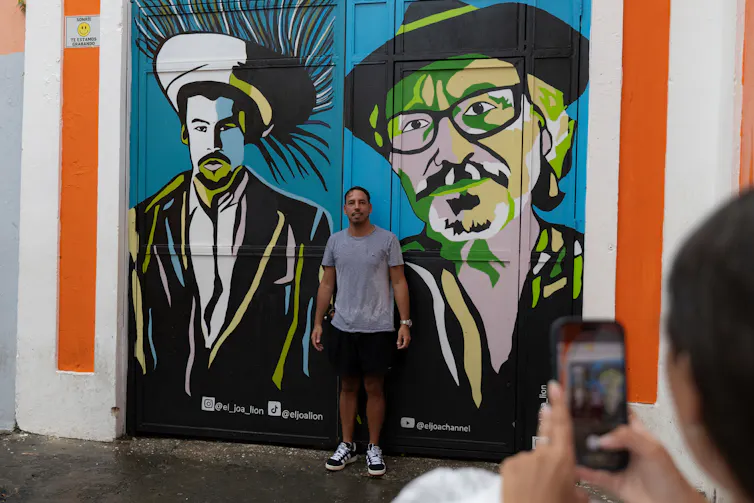 A man poses for a photo in front of a mural of Bad Bunny