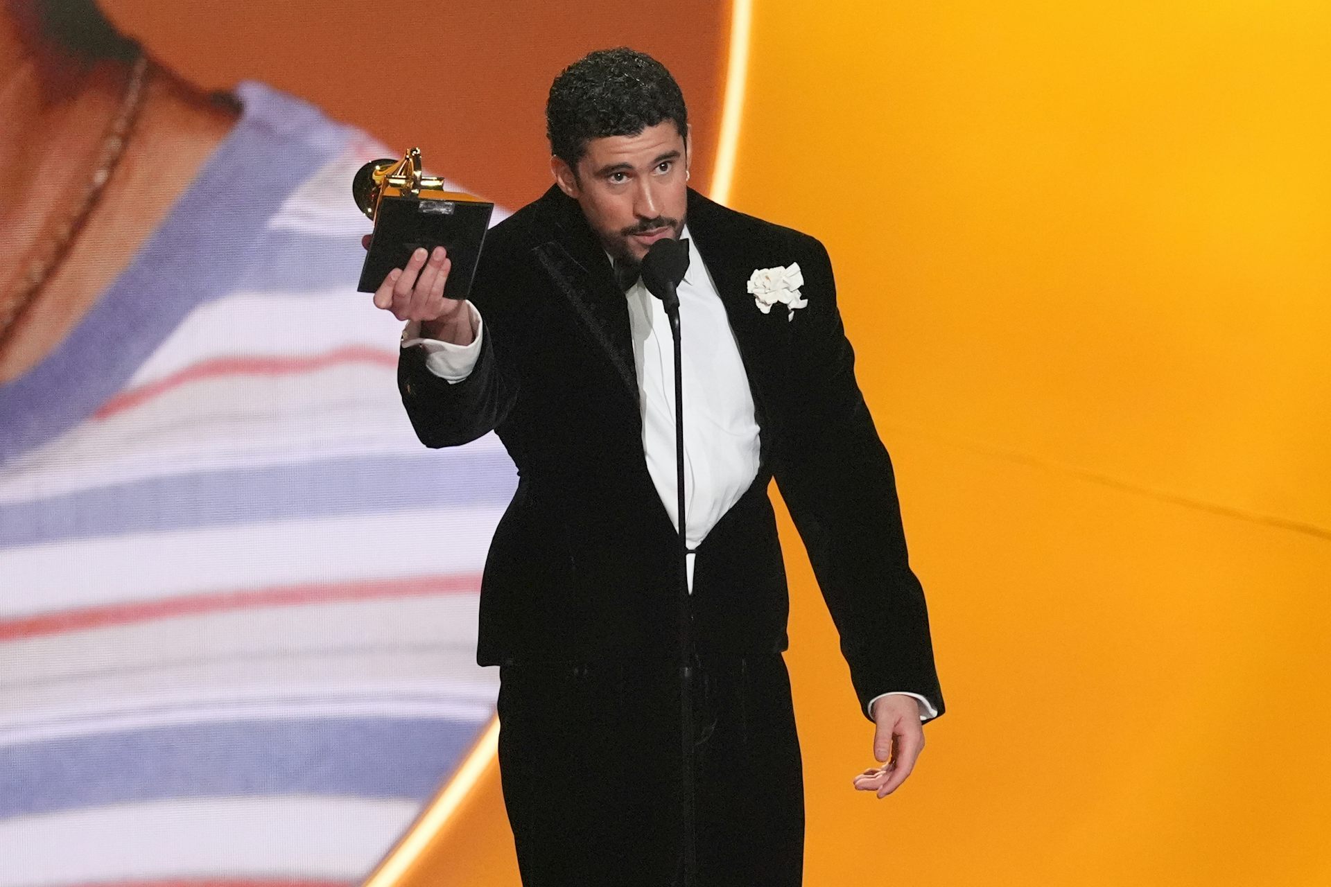 Un puertorriqueño con esmoquin negro habla por un micrófono mientras sostiene un trofeo Grammy.