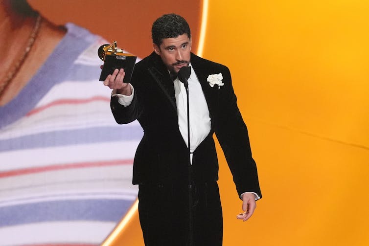 Un puertorriqueño con esmoquin negro habla por un micrófono mientras sostiene un trofeo Grammy.