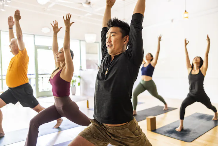 Diverse group of students doing crescent lunge pose during a yoga class.