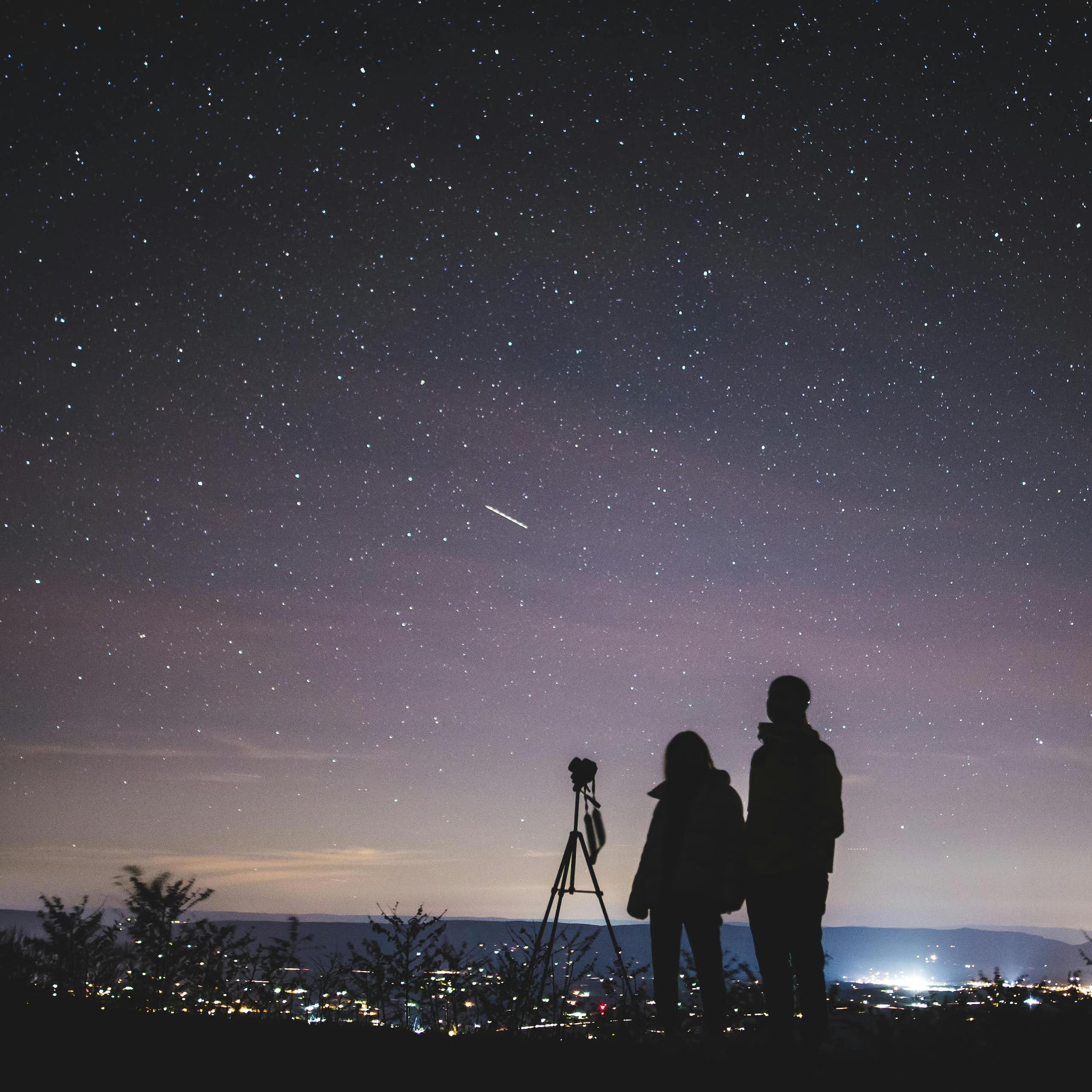 Silhouette of two people stargazing.
