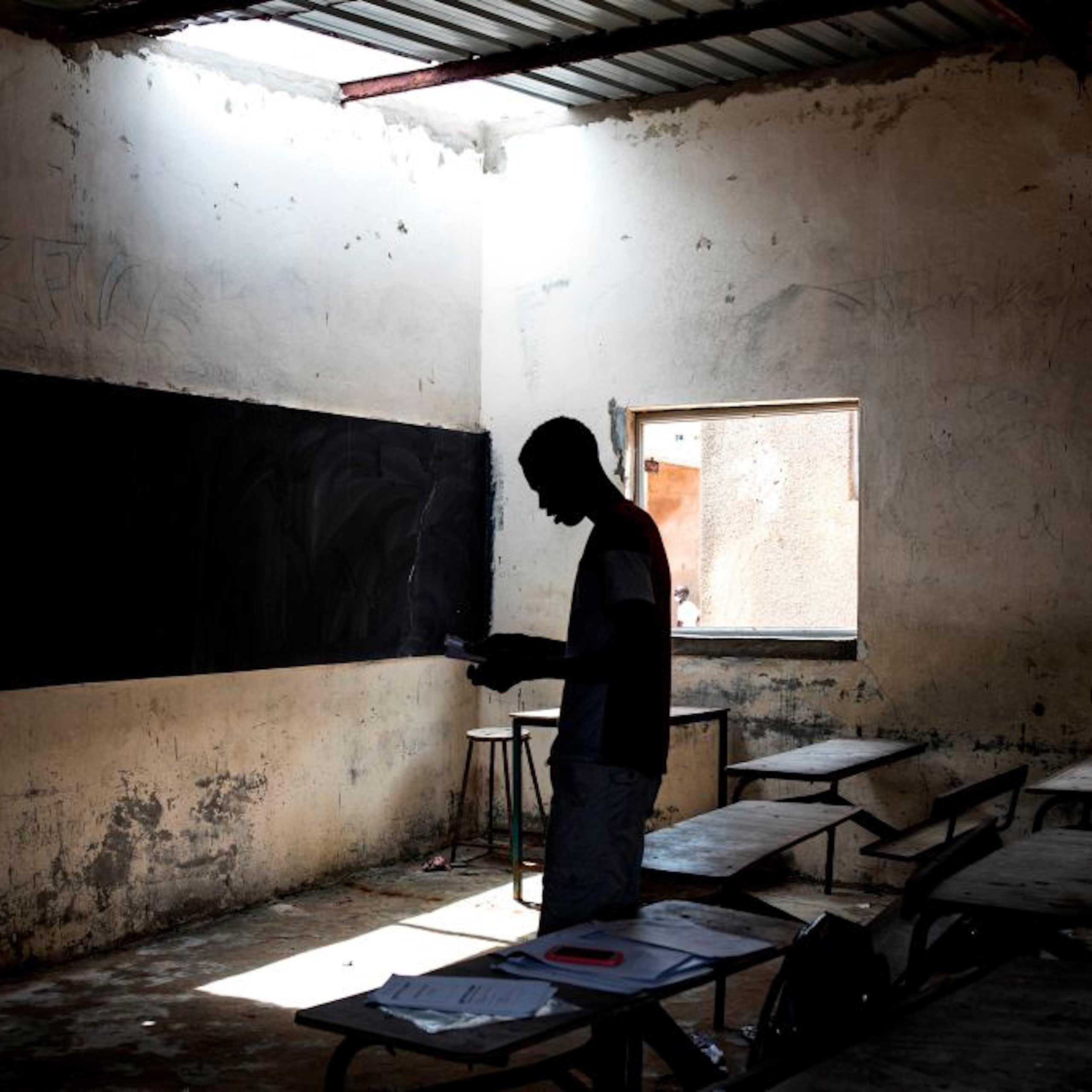 A person standing in a dilapidated classroom